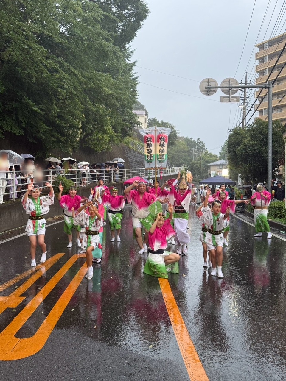 ゲリラ豪雨のなか傘を差して見ている観客と演舞中の連